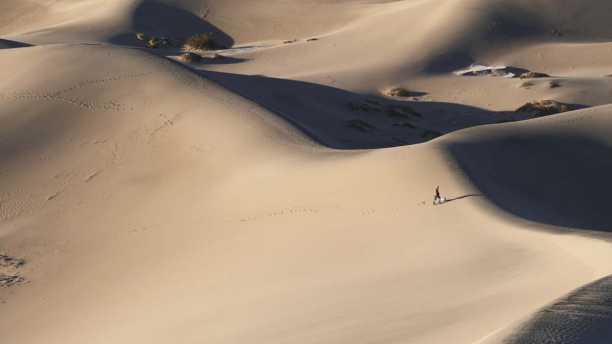 brown person walking alone in middle of desert dune